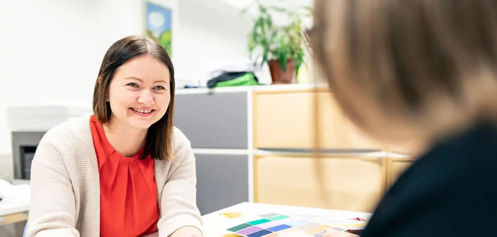 Hymyilevä nainen toimistossa käymässä läpi uravaihtoehtoja värikkäiden materiaalien kanssa